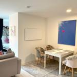 Essbereich mit weißem Tisch und vier Stühlen, Wandbild mit Herz, Sofa und Schlafzimmer im Hintergrund.