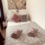 Ein Bett mit Musterdecke, Kissen und gefalteten Handtüchern. An der Wand hängt ein Bild.