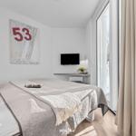 Schlafzimmer mit Bett, Wandbild und TV. Große Glastür führt auf Balkon.