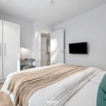 Schlafzimmer mit Bett, Kleiderschrank und TV. Tür führt in die Küche.