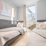 Zwei Betten mit grauem Kopfteil und gemusterten Bettwäsche. Fenster mit Blick auf Außenbereich.