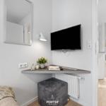 Schlafzimmer mit Fernseher, Spiegel und Schreibtisch. Blick in Wohnbereich mit Sofa.