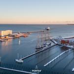 Hafen mit Segelschiff, Yachten und modernen Gebäuden am Wasser.
