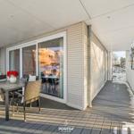 Terrasse mit Tisch, Stühlen und roten Blumen. Durchgehende Glasfront zum Innenraum.