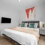 Schlafzimmer mit Bett, Wandbild und Fernseher an der Wand.