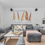 Wohnbereich mit grauem Sofa, Küchenzeile und Wandbild mit Segelbooten.