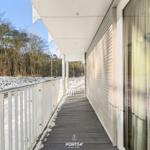 Eine überdachte Terrasse mit weißer Brüstung und schneebedecktem Boden führt entlang eines Hauses.