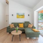 Ein Wohnzimmer mit grünem Sofa, Holzboden und großem Fenster zur Terrasse.