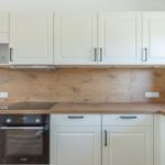 Küche mit weißen Schränken, Holzoberflächen und integriertem Ofen.