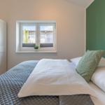 Schlafzimmer mit Bett, Fenster und grüner Wand. Wandbild mit Schmetterling.