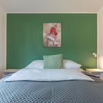 Schlafzimmer mit grünem Akzentwand, Bett und Wandbild mit Schmetterling.