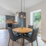 Essbereich mit runden Tisch und Stühlen, Küche mit grauen Schränken und Holzboden.