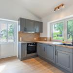 Küche mit grauen Schränken, Holzoberfläche und Fenster zur Außenseite.