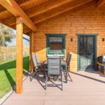 Terrasse mit Tisch, Stühlen und Hundehütte vor Holzhaus mit grünen Fenstern.