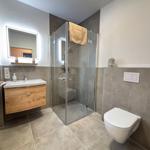 Bathroom with shower, sink, and toilet. Wooden vanity and lit mirror.