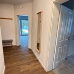 Hallway with wooden floor, mirror, and door. Passageway to living area with glass door.