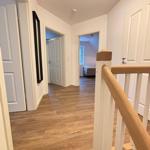 Hallway with wooden floor and staircase to upper floor. Doorways to bedrooms and bathroom.