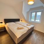 Bedroom with double bed, wooden floor, and window. Ceiling light and bedside table visible.