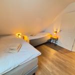 Two beds with white bedding and towels. Wooden floor and sloped ceiling.