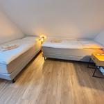 Two beds in an attic room with wooden floor and wall lamps.