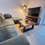 Living room with sofa, coffee table, and TV. Large window view to outdoor area.