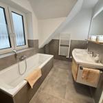 Bath with shower, sink and window. Sloped ceiling and gray tiles.