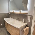 Bathroom with double sink, lit mirror, and wooden vanity.