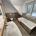 Bathroom with bathtub, sink, and toilet under sloped ceiling.