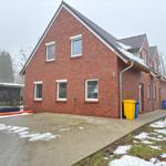 Red brick house with snow on roof and ground. Front side with windows and trash bins.