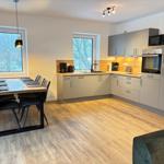 Kitchen with dining table, two windows, and wooden floor. Appliances and furniture are present.