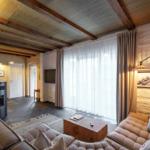 Wohnzimmer mit Sofa, Kamin und großen Fenstern. Steinwände und Holzbalken.