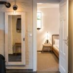 Flur mit Schlafzimmer und Spiegeltür. Bett, Nachttisch und Wandbeleuchtung sichtbar.