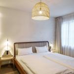 Schlafzimmer mit Doppelbett, Wandlampe und Deckenleuchte. Fenster mit Vorhängen.