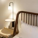 Ein Bett mit Holzgestell und weißer Bettwäsche neben einer Stehlampe und einem Stuhl.