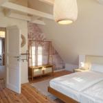 Schlafzimmer mit Dachschräge, Bett, Kleiderständer und Tür zu angrenzender Raum.