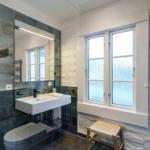 Badezimmer mit Waschbecken, Spiegel, Toilette und Fenster.