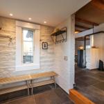 Eingangsbereich mit Steinwand, Holzbank und Fenster. Blick in den Flur mit Kamin und Spiegel.