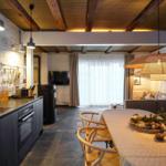 Küche mit Esstisch, Wohnbereich mit Sofa und Fernseher, weiße Ziegelwände und Holzbalkendecke.