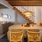 Essbereich mit Tisch und Stühlen, dahinter Wohnbereich mit Sofa und Treppe.