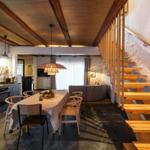 Essbereich mit Tisch, Stühlen und Küchenzeile. Holztreppe führt zur oberen Etage.