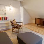 Wohnraum mit Holzboden, Sessel, Couch und Radio-Schrank unter Dachschrägen.