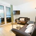 Wohnzimmer mit braunen Ledersofas, Fernseher und bodentiefen Fenstern zur Terrasse.