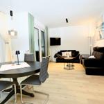 Wohn- und Essbereich mit Esstisch, Sofa und Fernseher. Holzboden und große Fenster.