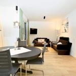 Wohn- und Essbereich mit Esstisch, Sofa und Fernseher. Holzboden und große Fenster.