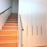 Helle Treppe mit Holzstufen und Metallgeländer neben weißen Schranktüren.