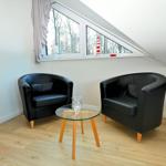 Zwei schwarze Sessel und ein Glas-Tisch stehen vor einem Dachfenster.