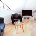 Wohnzimmer mit Sofa, Sessel, Glas-Tisch und Fernseher unter Dachschrägen.