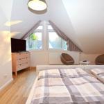 Schlafzimmer mit Doppelbett, zwei Sesseln, TV und Fenster mit Blick auf Dächer.