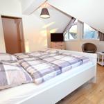 Schlafzimmer mit Dachschrägen, Bett, Fernseher und zwei Stühlen.