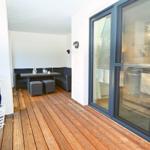 Terrasse mit Holzboden, Sitzgruppe und Tisch. Durchgehende Glastüren zum Innenraum.